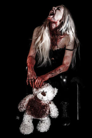 Bloody young woman holding a teddy bear over black backgroundの写真素材