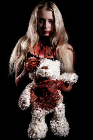 Bloody young woman holding a teddy bear over black backgroundの写真素材