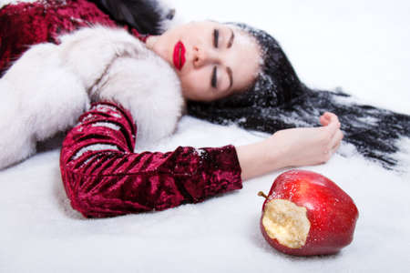 Pretty young woman laying on a snow near the red bitten appleの写真素材