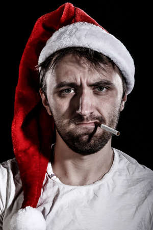 Unshaven man in a Christmas hat smoking a cigarette over black backgroundの写真素材