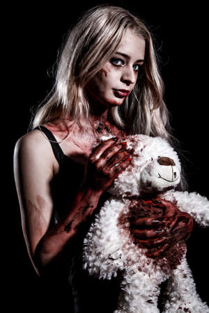 Bloody young woman holding a teddy bear over black backgroundの写真素材