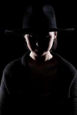 Young woman in a black hat over black backgroundの写真素材