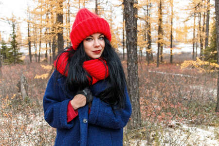 Pretty young woman in a red hat and scarf walking in the forest