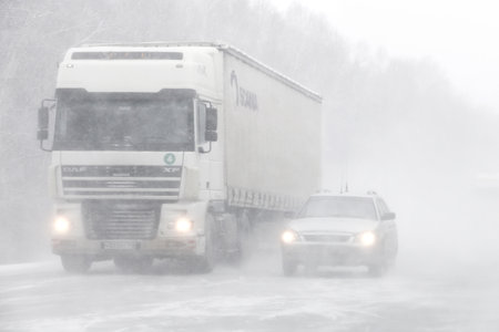 Chelyabinsk region, Russia - February 10, 2018: Semi-trailer truck DAF XF and motor car Lada Priora at the interurban road during a heavy blizzard.のeditorial素材
