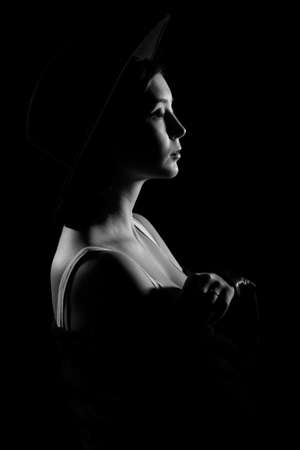 Beautiful young woman in a black hat in the darknessの写真素材