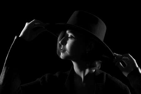 Beautiful young woman in a black hat in the darknessの写真素材