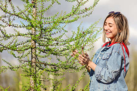 Smiling young girl near the conifer tree in the early spring