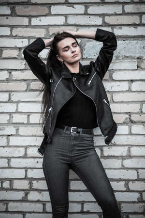 Young woman in a black leather jacket at the background of a brick wallの写真素材