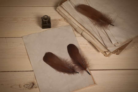Brown goose feathers, ink bottle and empty old papers laying on the wooden deskの写真素材