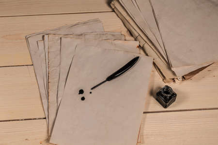 Black goose feather, ink bottle and empty old papers laying on the wooden deskの写真素材