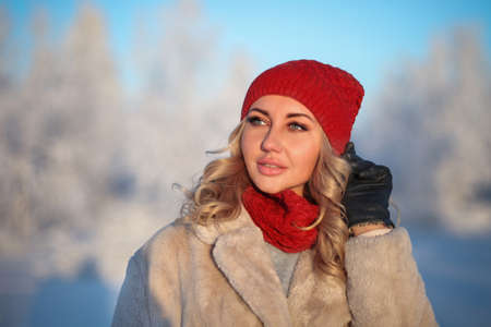 Portrait of the young woman in a warm knitted hat and a snood in the winter forest