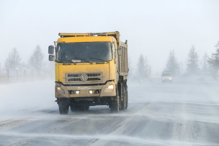 Novyy Urengoy, Russia - April 20, 2022: Yellow dump truck DongFeng DFL3251 in a city street during a strong wind and snowfall.のeditorial素材