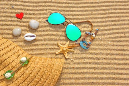 Sunglasses, Fashion Straw Hat, shells, stones and wooden heart on the beach sand  Marine Summer...