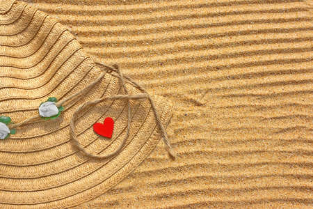 Vintage Fashion Straw Hat and small wooden love heart on the beach sand の写真素材