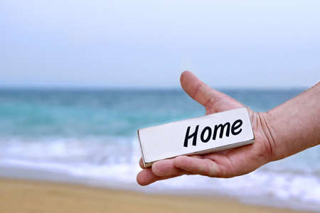 Male Hand with HOME signboard. Sea, Beach and summer in the background.の写真素材