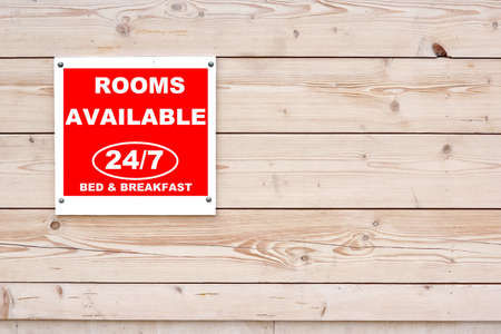 ROOMS AVAILABLE 24/7 BED & BREAKFAST Red White Sign on Timber Wall Background ROOMS AVAILABLE 24/7 BED & BREAKFAST Red White Sign on Timber Wall Background