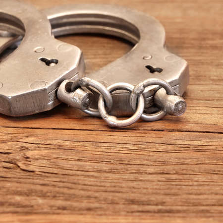 Steel Handcuffs on Wooden Table. Background with space for text or image.の写真素材