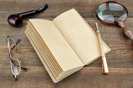 Open Vintage Notebook With Blank Pages, Gold Fountain Pen, Glasses, Retro Magnifier, Compass and Smoking Pipe On Grunge Woodeen Table Backgroundの写真素材