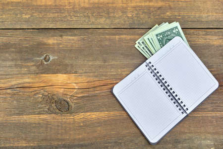 Open Notebook With Checkered White Pages and One USA Dollar Bills On Grunge Wood  Textured Background With Copy Space For Text or Image. Overhead Viewの写真素材