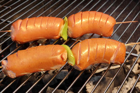 Four Tasty Sausages On The Hot Barbecue Charcoal Grill Close-up. Good Snack For Summer Outdoor BBQ Party Or Picnicの写真素材