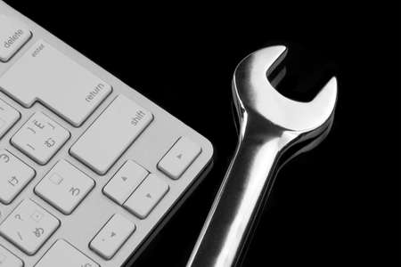 Chrome Plated Wrench And  Wireless Keyboard Isolated On Black Glass Background With Reflection. Remote Assistance Or Technical Support Or Repair Service Or Bug Fix  Or Business Solutions Conceptの写真素材