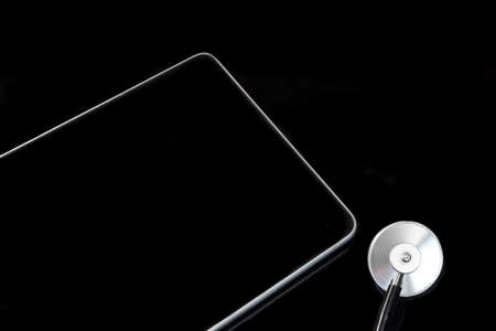 Close-up Of Modern Tablet Computer And Stethoscope Head Isolated On Black Glass  Background With Reflection. High Angle Viewの写真素材
