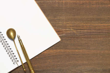 Opened Spiral Bound Notebook With Blank White Pages, Vintage Old Spoon And Gold Fountain Pen  On The Rustic Rough Brown Wooden Tableの写真素材