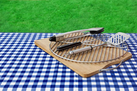 Picnic Table Covered Checkered Blue White Tablecloth And BBQ Grill With Tools Kit, Park Lawn In The Backgroundの写真素材