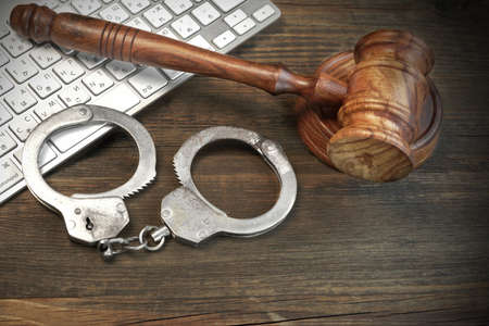 Cyber Crime Concept, Judges Gavel Computer Keyboard  And Real Handcuffs On The Rough Brown Wood Tableの写真素材