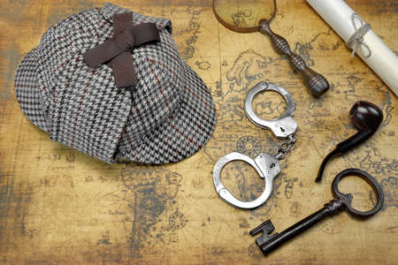 Overhead View Of Sherlock Holmes Deerstalker Hat  And Private Detective Tools On The Old World Map Background. Items Include Vintage Magnifying Glass, Retro Key, Manuscript, Smoking Pipe,  And Handcuffsの写真素材