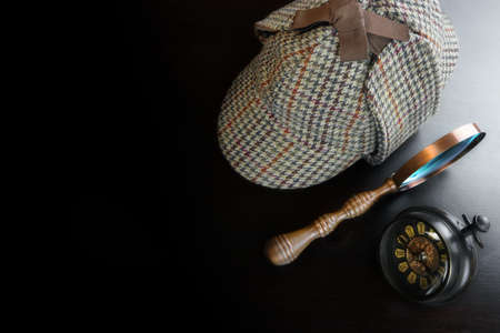 Sherlock Holmes Deerstalker Hat And Vintage Clock And   Magnifying Glass On The Black Wooden Table Background. Overhead View.  Investigation Concept.の写真素材