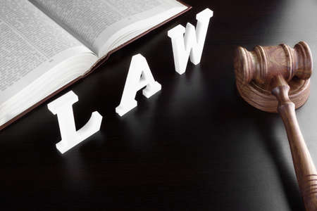 Judges Gavel, Red Open Legal Book And White Sign LAW From Wood Latter On The Black Table In The Back Light. Overhead View.の写真素材