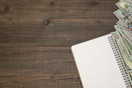 Opened Spiral Notepad With Blank White Page And Dollar Cash On The Rough Rustic Wood Table...