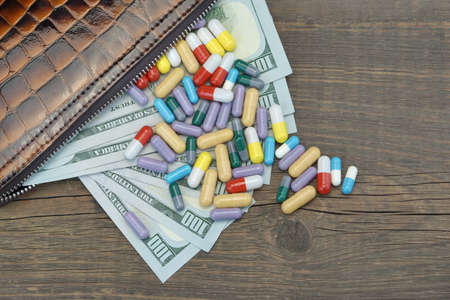 Wallet With US Dollar Cash And Scattered Pills On The Rough Wood Background, Top View, Conceptual Imageの写真素材