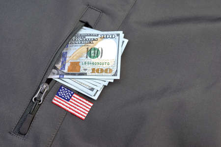 Money American Dollar Pile Stuck Out Of Military Khaki Coat or Bag Pocket With American Flag Patch