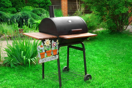 Barbeque Charcoal Grill Appliance With Sign Welcome In Decorative Backyard Garden On The Lawnの写真素材