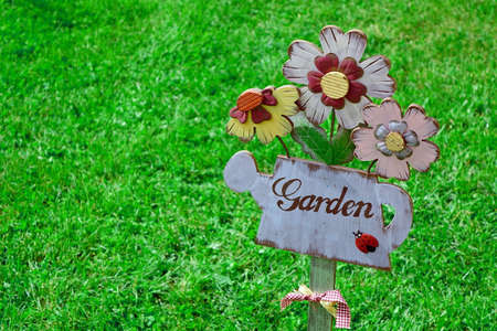 Close-Up Of Wooden Plaque In The Shape Of A Watering Can And Garden Sign. Backyard Garden Lawn In The Backgroundの写真素材