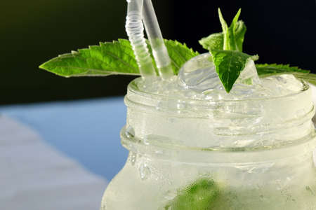 Close Up Of Misted Glass Mason Jar With Mojito Cocktail On The Table, Popular Summer Drink, Mixed With Rum, Soda Water, Cracked Ice,  Lime Wedges And Mint Sprigの写真素材