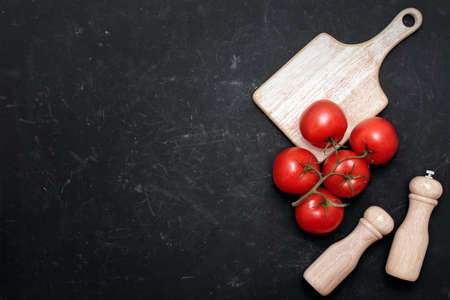 Ripe Red Tomatoes On Branch, Paper And Salt Mill On The White Wooden Cutting Board On Black Background.の写真素材