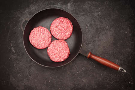 Raw Minced Homemade Grill Beef Burgers in Frying Pan, Top View. Griddle Grill Pap and Ground Beef Meat Patties for Grilling on Black Background, Overhead View. Raw Steak Burgers Cutlets On Grill Pan.の写真素材