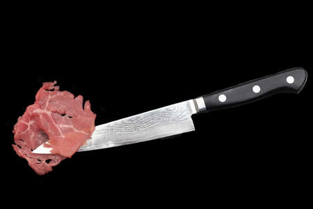 Carpaccio Slice and Japanese Damascus Stainless Steel Chef Knife Isolated On Black Background, Front View. Marbled Beef Carpaccio On Sharp Kitchen Knife.の写真素材