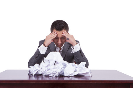 Image of a tensed young businessman with crumpled papers on his deskの写真素材