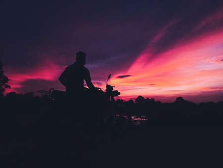 Silhouette of a man on a motorcycle in the sunset.の写真素材