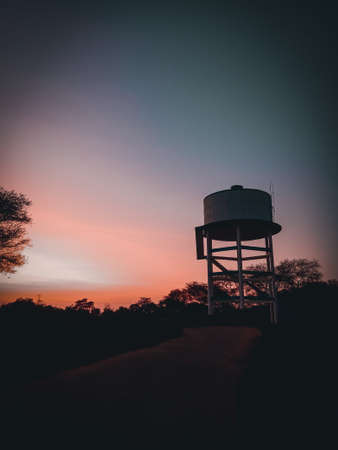 A vertical shot of a water tower on a hill under a colorful sunsetの写真素材