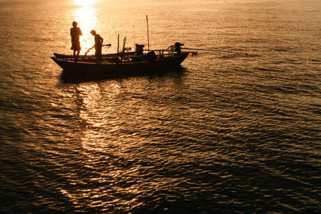Silhouettes fishing boats and fisherman in the sea after sunsetの写真素材