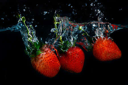 fresh strawberry dropped into water with splash on black backgroundsの写真素材