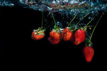 fresh strawberry dropped into water with splash on black backgroundsの写真素材
