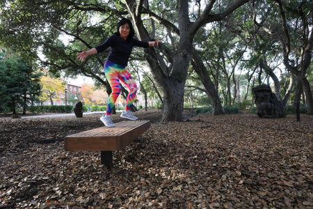 Photo of a mature Vietnamese woman jumping of a bench in a parkの写真素材