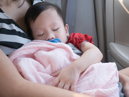 Baby sleep in car with dummy in mouth. Asian toddler sleep in her mom hand.の写真素材