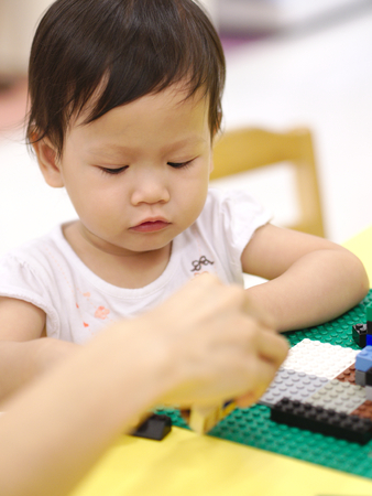 Asian baby playing puzzle toys with parent on yellow table indoorの写真素材